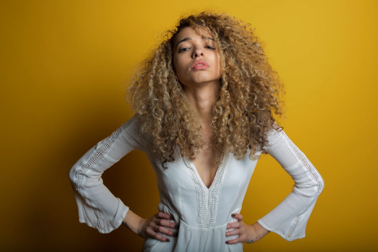 Woman with curly hair wearing a white dress against a yellow background