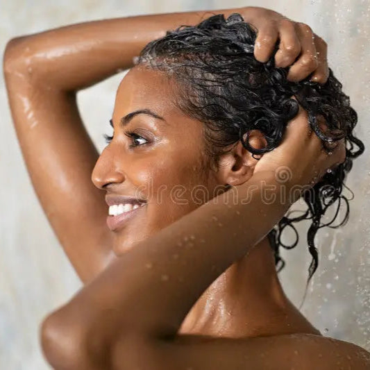Woman washing her hair under a shower with water droplets visible